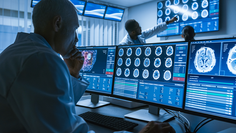 Ein Arzt begutachtet CT-Scans auf einem Raum voller Bildschirme.